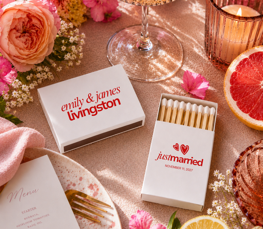 Personalized matchboxes with 'just married' text on a table setting with flowers and a glass.