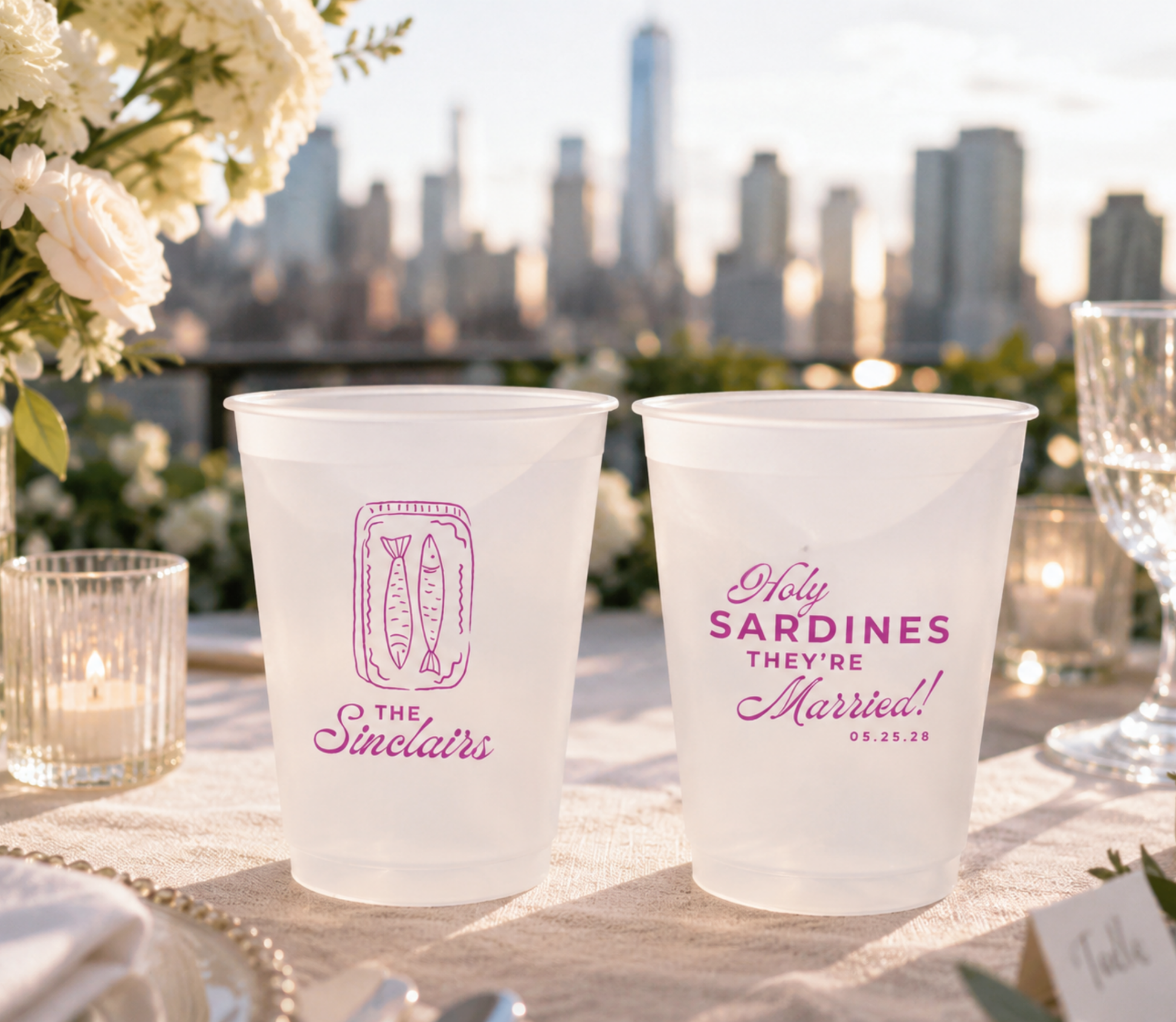 wedding coastal city Frosted cups with pink text on a table outdoors with a city skyline in the background.