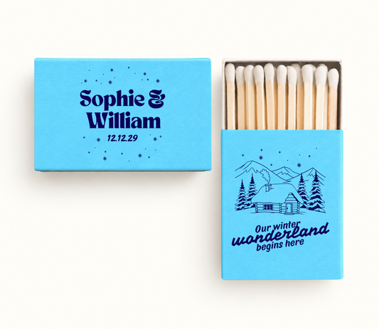 Personalized blue Our Winter Wonderland Christmas wedding matchboxes featuring navy snowy cabin artwork, Sophie and William names, and wedding date.