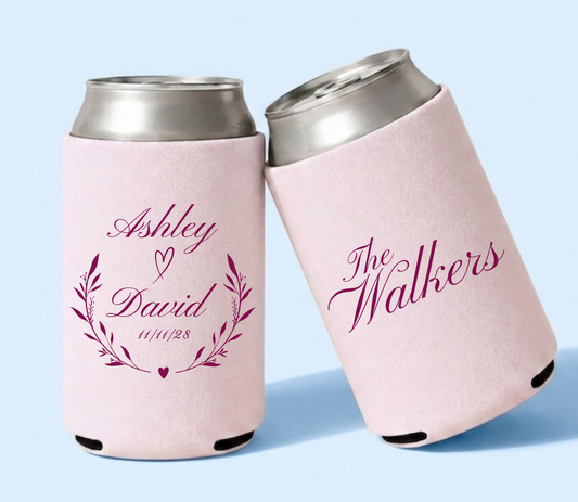 Personalized blush pink wedding can coolers featuring Ashley and David names framed by botanical branches and heart details with The Walkers family name in berry pink lettering.