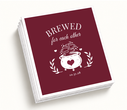 Personalized Brewed for Each Other burgundy Halloween wedding cocktail napkins featuring a bubbling cauldron with heart artwork, botanical accents, and custom wedding date.