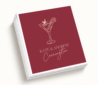 Personalized Christmas cocktail wedding napkins featuring burgundy background, ivory holiday cocktail illustration, candy cane detail, and custom wedding names.