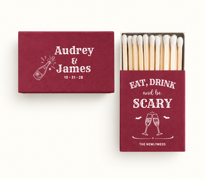Personalized burgundy Eat Drink and Be Scary wedding matchboxes featuring white champagne glasses, bats, Audrey and James names, and custom wedding date 10.31.28.