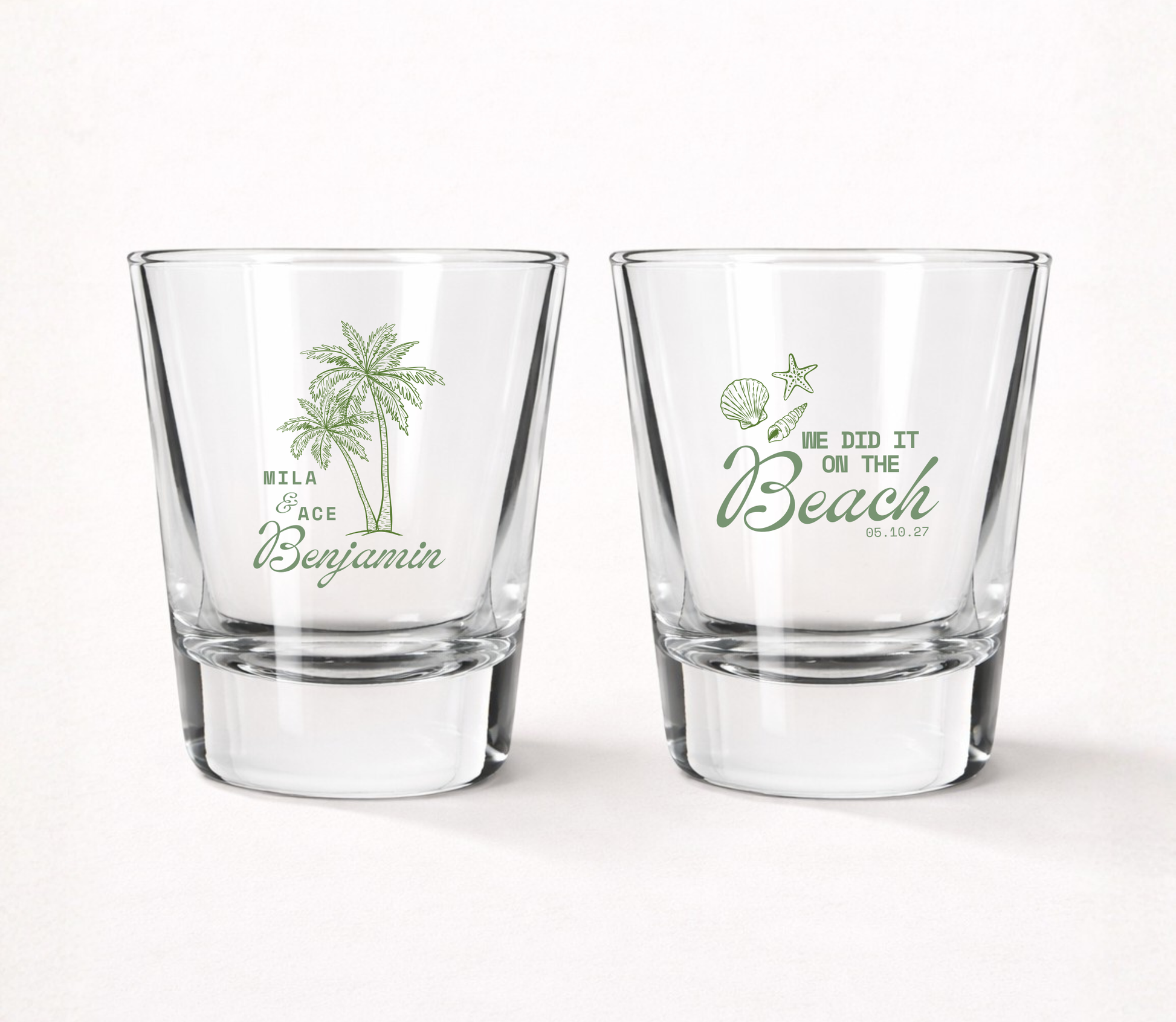 Clear personalized beach wedding shot glasses featuring tropical palm trees, custom couple names, beach themed artwork, and wedding date.