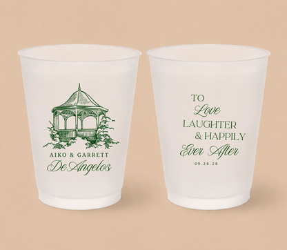 White frosted wedding cups featuring a custom gazebo venue illustration, couple names, family surname, romantic wedding quote, and wedding date.