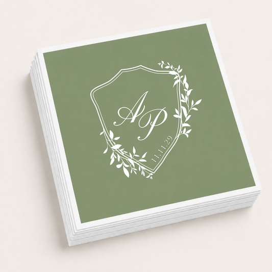 Sage green personalized wedding cocktail napkins featuring a botanical crest monogram with custom initials, wedding date, and elegant white print.