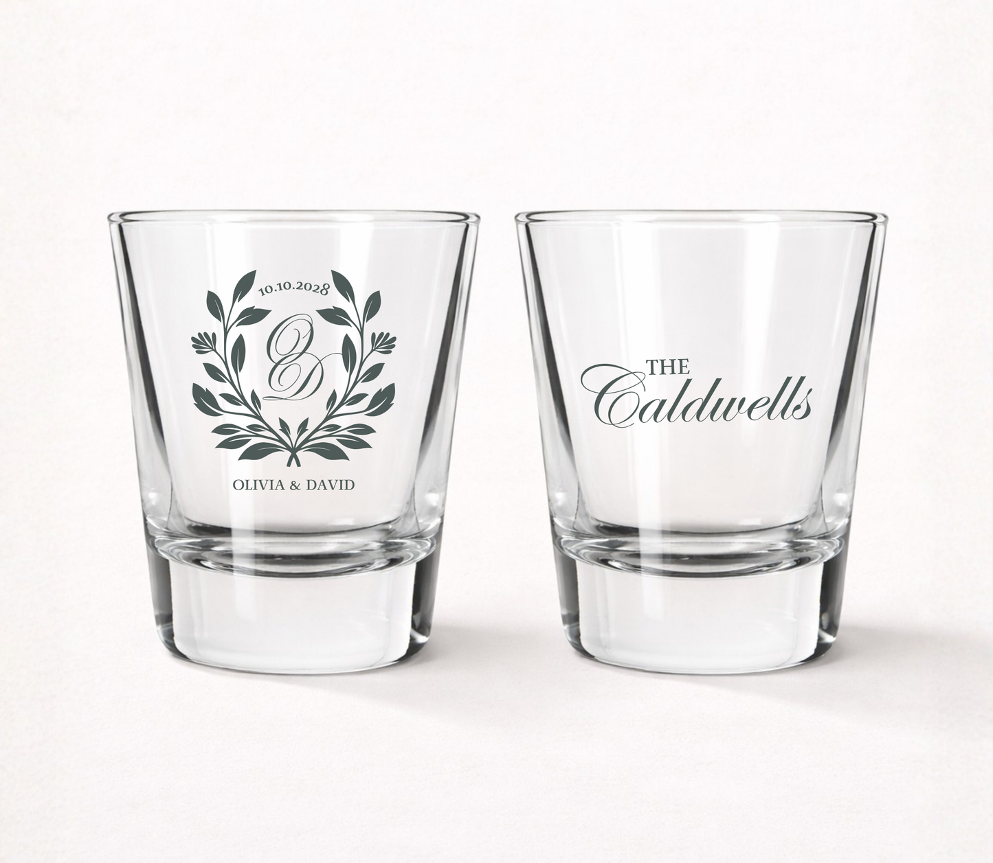 Personalized Laurel Crest wedding shot glasses featuring a custom monogram, botanical laurel wreath, couple names, family name, and wedding date.