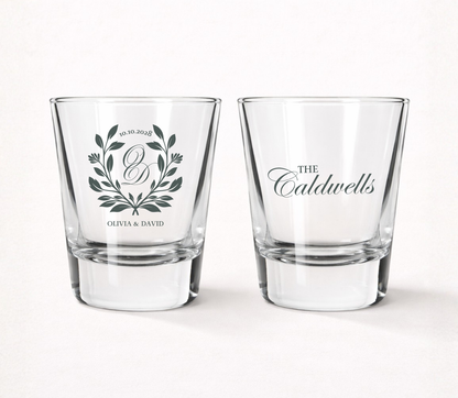 Personalized Laurel Crest wedding shot glasses featuring a custom monogram, botanical laurel wreath, couple names, family name, and wedding date.