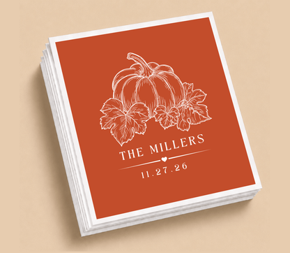 Personalized pumpkin Thanksgiving wedding table napkins featuring a white pumpkin and leaf illustration, custom family name, and wedding date on a terracotta background.