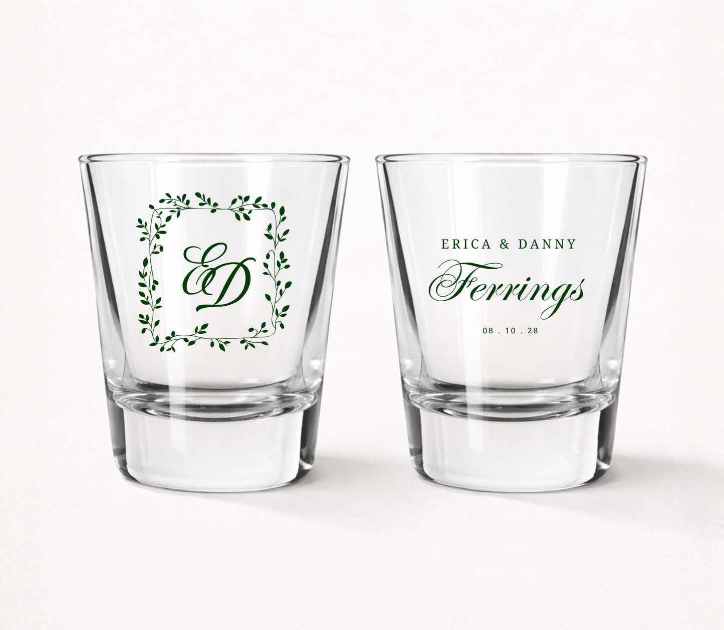 Personalized Ferrings Monogram wedding shot glasses featuring custom couple names, family name, monogram initials, wedding date, and botanical greenery frame.