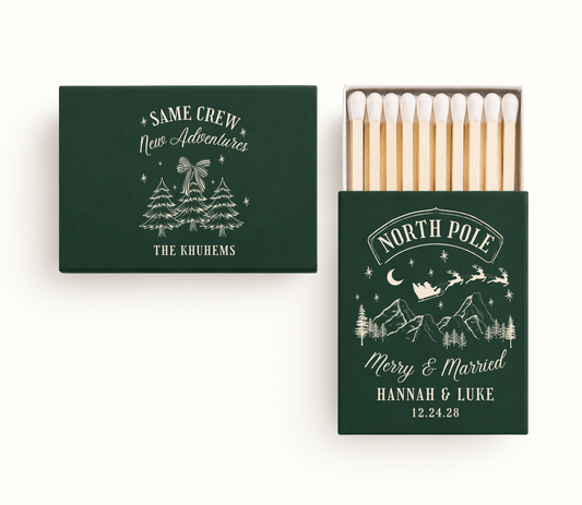Personalized evergreen North Pole Christmas wedding matchboxes featuring Santa sleigh, winter mountain artwork, Hannah and Luke names, and wedding date.