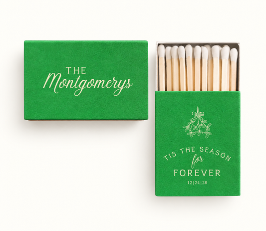 Personalized green Tis The Season For Forever Christmas wedding matchboxes featuring cream holiday greenery artwork, The Montgomery names, and wedding date.