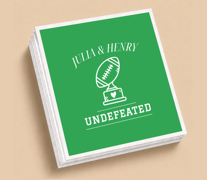 Personalized Undefeated football wedding napkins featuring a football trophy with a heart, green background, white lettering, and custom couple names.