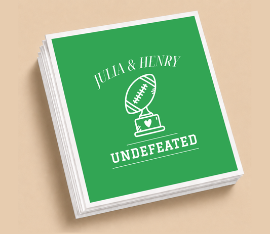 Personalized Undefeated football wedding napkins featuring a football trophy with a heart, green background, white lettering, and custom couple names.
