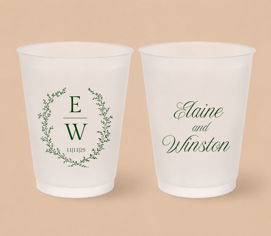 White frosted wedding cups featuring a botanical greenery wreath with custom initials E and W, wedding date, and personalized names Elaine and Winston.