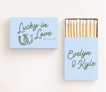 Light blue personalized wedding matchboxes featuring lucky horseshoe artwork, custom names Evelyn and Kyle, and wedding date