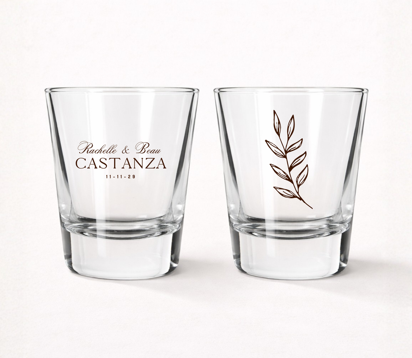 Clear personalized botanical wedding shot glasses featuring custom couple names, wedding date, and minimalist botanical leaf illustration.