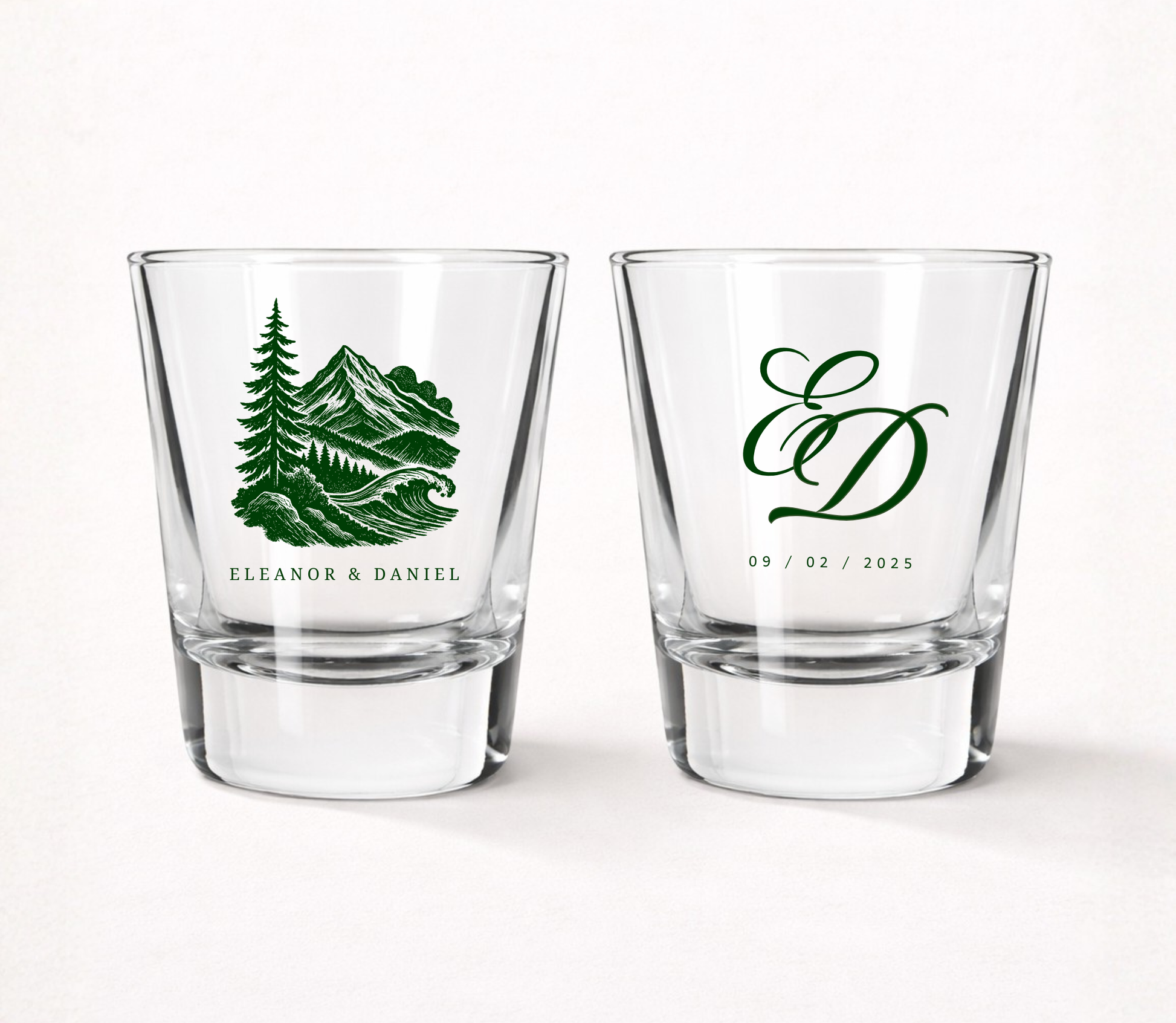 Clear glass wedding shot glasses featuring a scenic mountain landscape illustration with personalized couple names, elegant monogram, and wedding date.
