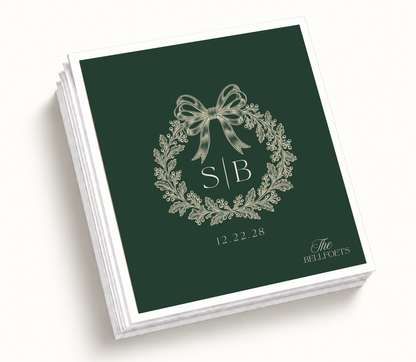 Personalized Christmas wedding napkins featuring a deep green holiday wreath, cream bow, custom initials, family name, and wedding date.