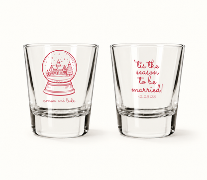 Personalized Tis The Season Christmas wedding shot glasses featuring a snow globe winter village, custom couple names, and wedding date.