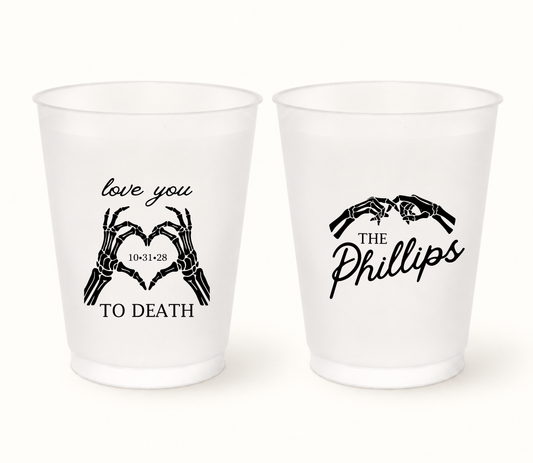 Personalized Love You to Death frosted Halloween wedding cups featuring black skeleton hands forming hearts, The Phillips last name, and wedding date 10.31.28.