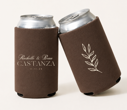 Personalized brown wedding can coolers featuring custom couple names, family name, wedding date, and elegant ivory botanical branch artwork.