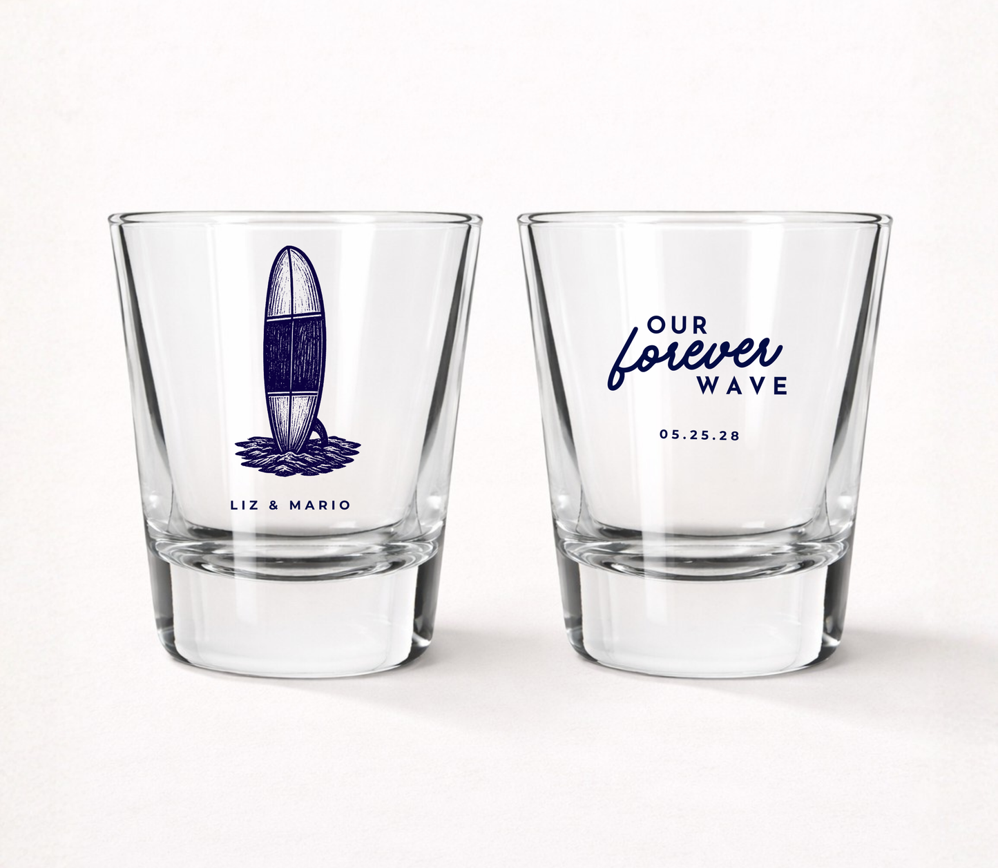 Clear glass wedding shot glasses featuring a vintage surfboard illustration with personalized couple names and Our Forever Wave wedding design.
