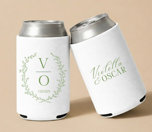 White personalized wedding can coolers featuring a botanical greenery wreath, custom initials V and O, wedding date, and personalized couple names Violetta and Oscar.
