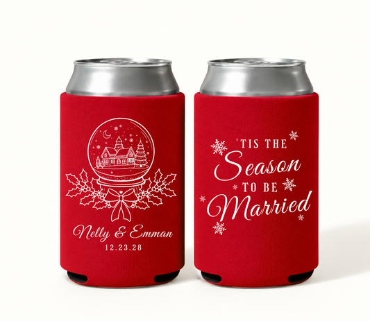 Personalized red Christmas wedding can coolers featuring a white snow globe village with holly and bow, Nelly and Emman names, wedding date 12.23.28, and ’Tis the Season to Be Married wording.