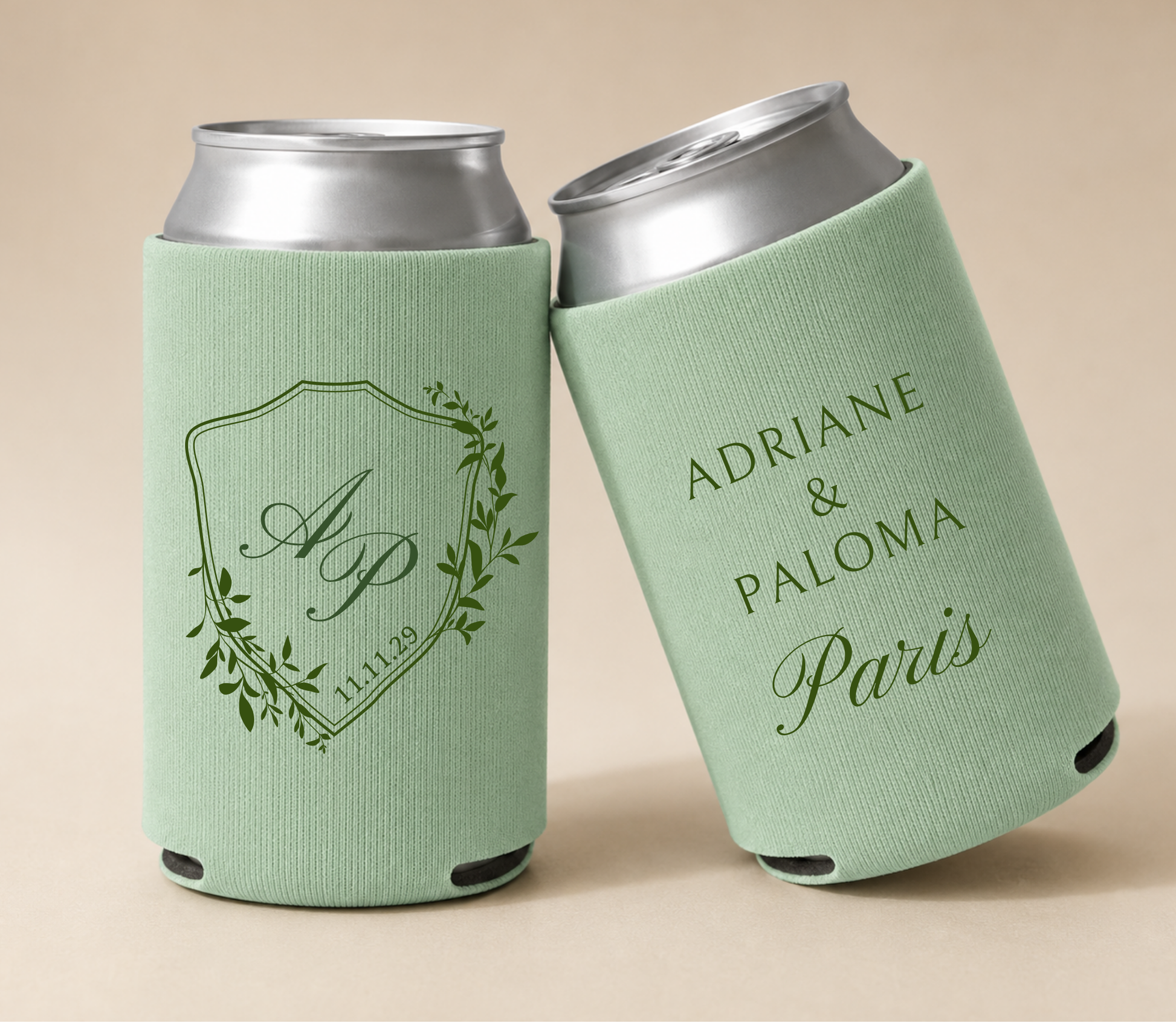 Sage green personalized wedding can coolers featuring a botanical crest with custom initials A and P, personalized couple names Adriane and Paloma, and wedding date.
