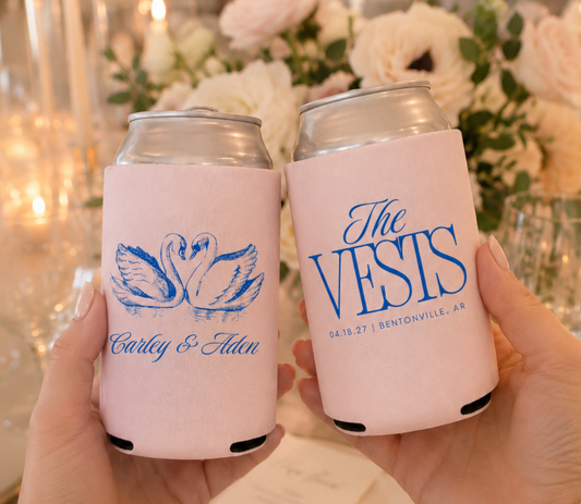 Two can coolers with personalized swan designs on a table with flowers and candles.