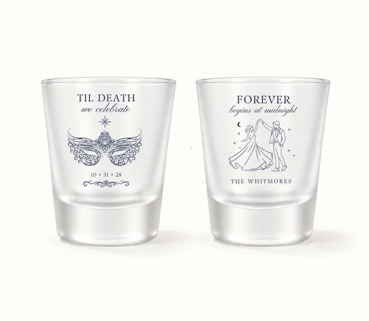 Personalized clear masquerade wedding shot glasses featuring navy Til Death We Celebrate wording, ornate mask, Forever Begins at Midnight design, dancing couple, The Whitmores surname, and wedding date 10.31.28.

