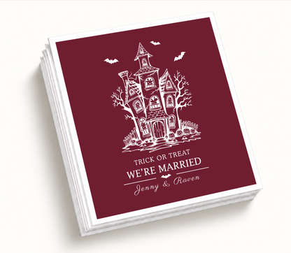 Personalized Trick or Treat We’re Married burgundy Halloween wedding cocktail napkins featuring a white haunted house, bats, pumpkins, and custom couple names.