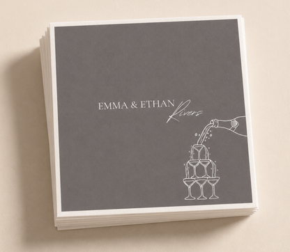 Personalized champagne tower wedding napkins with white pour artwork and custom couple names on charcoal gray napkins