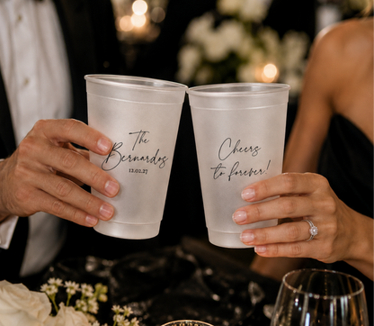 wedding couple holding a frosted cup with their last name, first names and date on them at their modern black tie wedding 