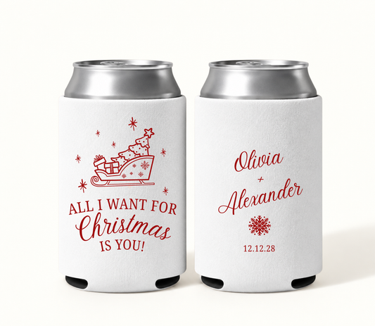 Personalized white All I Want for Christmas wedding can coolers featuring red Christmas sleigh artwork, Olivia and Alexander names, snowflake, and wedding date 12.12.28.