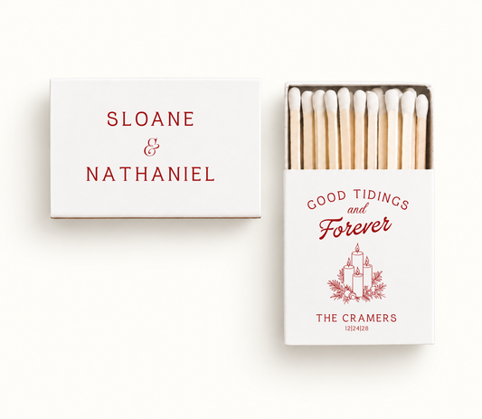 Personalized white Good Tidings and Forever Christmas wedding matchboxes featuring red candle and greenery artwork, The Cramers names, and wedding date 12.24.28.