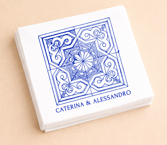 White personalized cocktail napkins featuring intricate Mediterranean blue tile artwork with custom names Caterina and Alessandro.