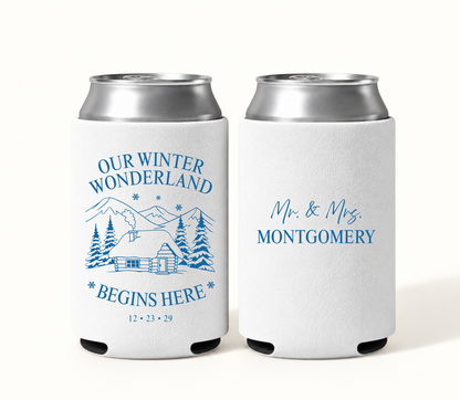 Personalized white Winter Wonderland wedding can coolers featuring blue snowy mountain cabin artwork, Our Winter Wonderland Begins Here wording, wedding date, and Mr. and Mrs. Montgomery design.