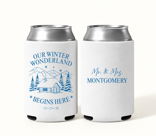 Personalized white Winter Wonderland wedding can coolers featuring blue snowy mountain cabin artwork, Our Winter Wonderland Begins Here wording, wedding date, and Mr. and Mrs. Montgomery design.