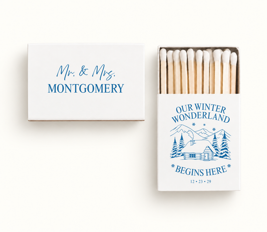 Personalized white Our Winter Wonderland wedding matchboxes featuring blue snowy cabin artwork, Montgomery names, and winter wedding date.