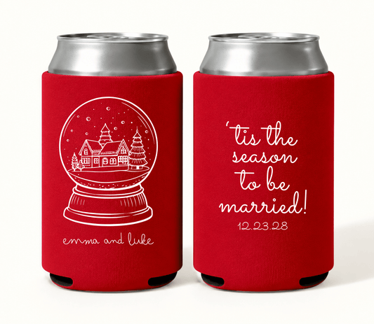 Personalized red Christmas wedding can coolers featuring a white Christmas village snow globe, Emma and Luke names, ’Tis the Season to Be Married wording, and wedding date 12.23.28.

