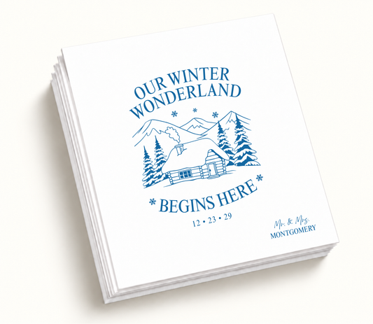 Personalized Our Winter Wonderland wedding napkins featuring snowy mountains, cabin illustration, pine trees, blue artwork, and wedding details.