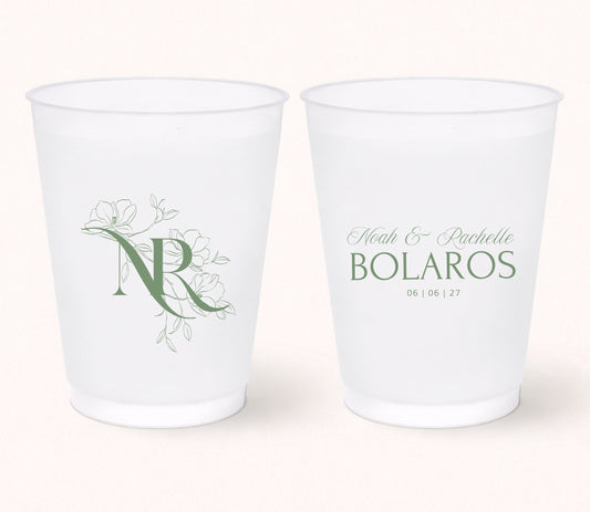 Two personalized frosted wedding cups featuring a floral monogram "NR" on one side and Noah & Rachelle Bolaros with the wedding date 06.06.27 printed in elegant sage green on the reverse.
Personalized wedding frosted cup featuring a floral monogram initial and elegant botanical artwork.
Custom monogram wedding drink cup with personalized couple names and wedding date.