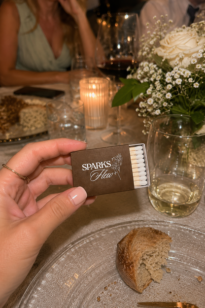 Person holding a wedding favor 'Sparks' matchbook at a rehearsal dinner with food and drinks.
